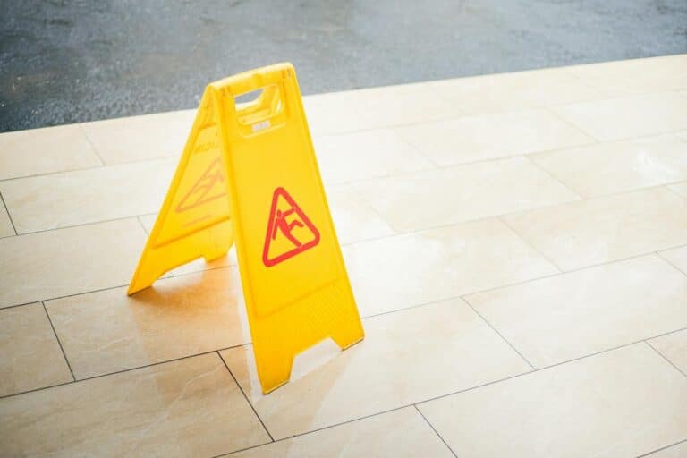 A bright yellow caution sign placed on a tile floor indicating a wet area for safety.