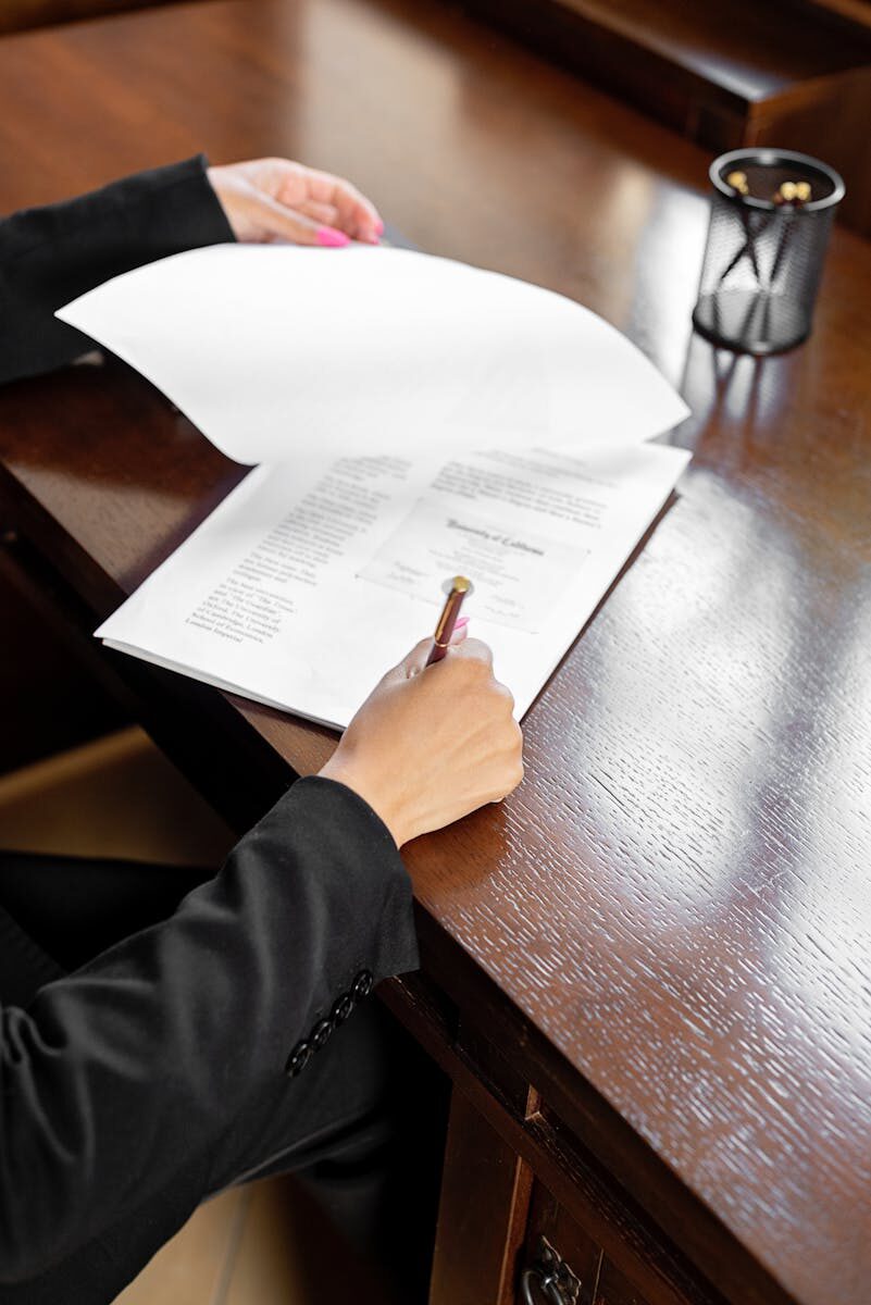 Close-up of a business professional signing a paper document at a wooden desk.